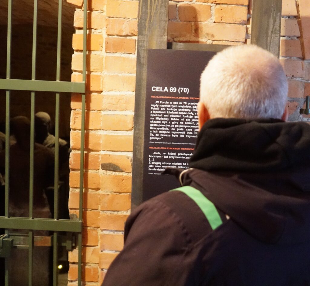 Starszy mężczyzna czyta wspomnienia zapisane na tablicy przy celi 69(70).
